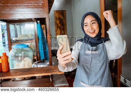 Veiled Woman Wearing An Apron Happily Looking At Her Cellphone