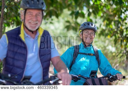 Active Caucasian Senior Couple With Electrobikes Standing Outdoors In The Park. Two Happy Elderly Pe