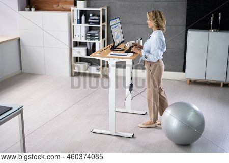 Woman Using Adjustable Height Standing Desk In Office For Good Posture