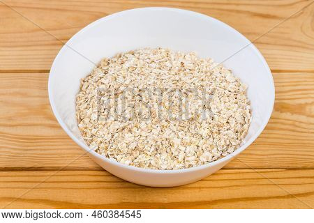 Raw Thin-rolled Oats In The White Bowl On A Rustic Table, Close-up In Selective Focus