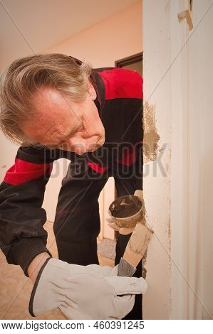 Older Man Working In Empty Apartment Repairing Holes In Walls