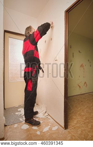 Older Man Removing Old Wallpapers Off The Walls In Empty Apartment