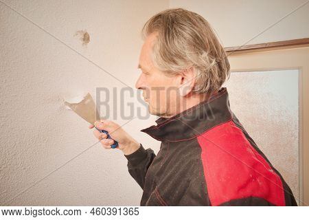 Older Man Removing Old Wallpapers Off The Walls In Empty Apartment
