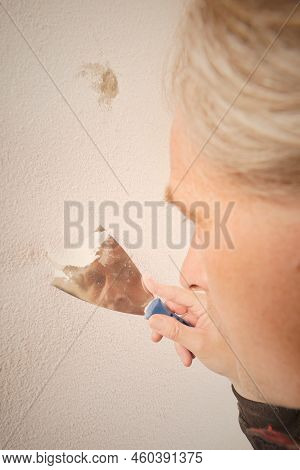 Older Man Removing Old Wallpapers Off The Walls In Empty Apartment