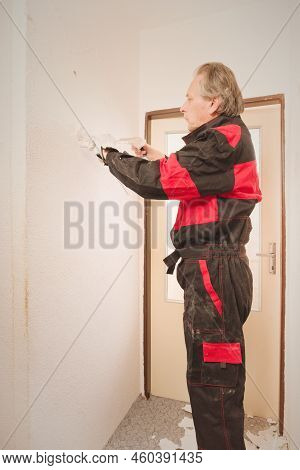 Older Man Removing Old Wallpapers Off The Walls In Empty Apartment