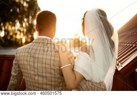 Happy Young Bride Woman In White Dress Running In The Sunset Light With Blowned Hair. Back View.