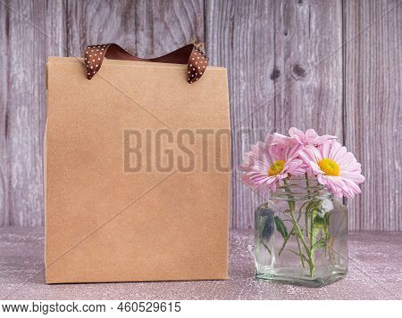 Brown Paper Bag Packaging With Ribbon Handles Placed On A Gray Stone Background With A Wooden Wall. 