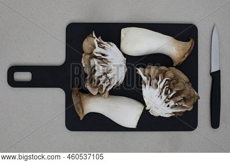 Top View On Trumpet And Oyster Mushrooms On Black Cutting Board With A Knife On The Side