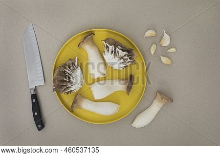 Cut In Half Trumpet And Oyster Mushrooms On Yellow Plate With A Knife And Garlic Cloves Top View