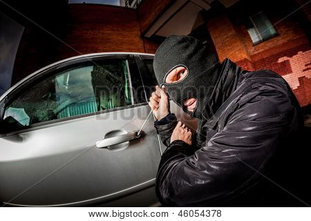 Røver og biltyv i en maske åbner døren til bilen og kaprer bilen.