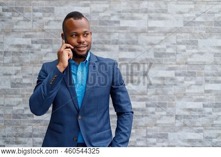 Smiling Elegant Male Boss With Hand In Pocket Talking Over Mobile Phone While Standing Against Brick