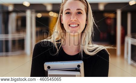 Portrait Of Smiling Beautiful Young Woman With Blond Hair Carrying Laptop Standing In College Campus