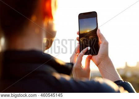 Midsection Of Young Caucasian Woman Photographing Sunrise Over Mountain With Smartphone Against Clea