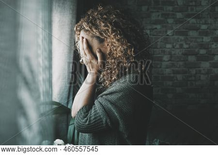 Sad And Worried Woman Side Portrait At Home In The Dark Looking Outside The Window. Worried And Lone