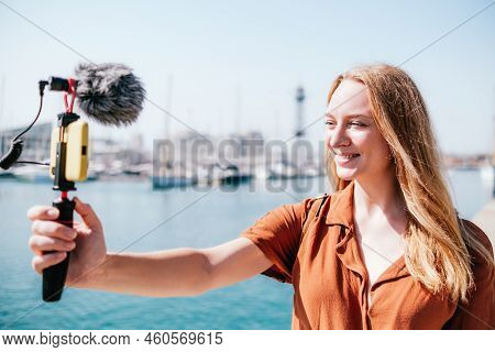 Female Travel Vlogger Streaming Near Sea In A Touristic Destination. She Looks To Her Smart Phone Sm