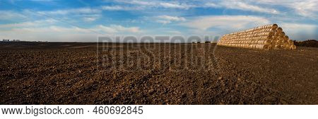 Panoramic View Of Straw Bales Stacked In A Pyramid Shaped Pile On A Plowed Field, Arable Land