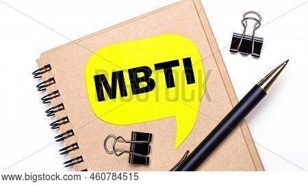 On A Light Background, A Brown Notebook, A Black Pen And Paper Clips, And A Yellow Card With The Tex