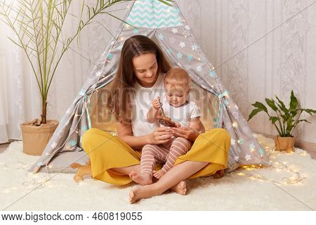 Indoor Shot Of Attractive Dark Haired Woman Wearing White T Shirt Sitting In Peetee Tent With Her In