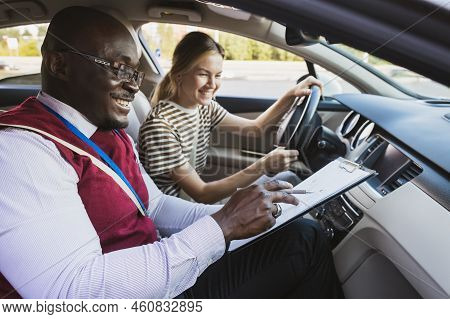Driving School Concept. A Car Instructor Teaches A Young Woman How To Drive. Teaching The Rules Of T