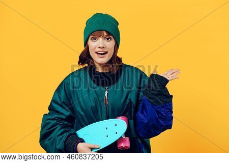 A Joyful Woman Stands On A Yellow Background In A Fashionable Jacket And Hat From The 90s And Holdin