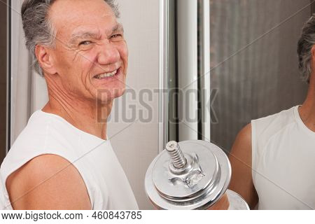 Mature Man 60plus Working Out With Weights At Home In Front Of A Mirror Doing Bicep Curls