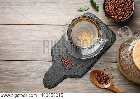 Cup Of Freshly Made Aromatic Buckwheat Tea And Granules On Wooden Table, Flat Lay. Space For Text