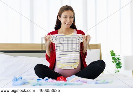 A Big Pregnant Woman Is Happily Preparing Baby Clothes On Her Stomach. A New Mother Is Waiting To Gi