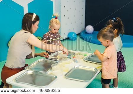 Sensory Play At Multi-cultural Nursery School. Toddlers With Their Teacher Playing With Striped Stra
