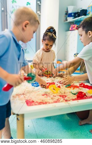 Fun Sensory Play With Moldable Kinetic Sand At Nursery School. Toddlers Standing Around The Table An