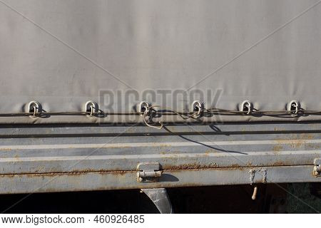 A Piece Of  Tarpaulin On A Iron Gray Side Of A Car Trailer With An  Cable In The Loops