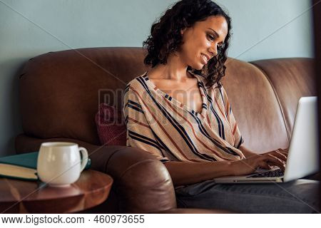 Young Woman Sitting On The Couch Working On Laptop. African Female Working On Laptop Computer At Hom