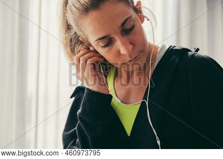 Mid Adult Female Runner Wearing Earphones And Using Smartphone While Sitting On Bed In Apartment Dur