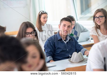 Happy highschool boy sitting with classmates in schoolroom