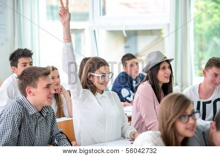 Happy schoolgirl raising hand during lecture in schoolroom