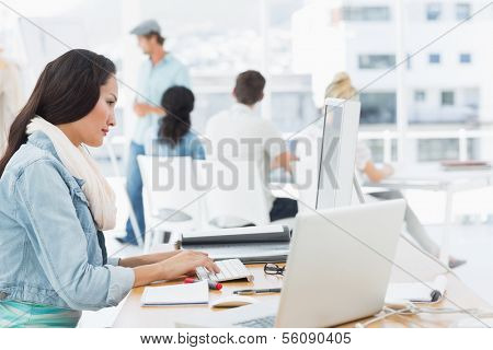 Casual woman using computer with group of colleagues behind in a bright office