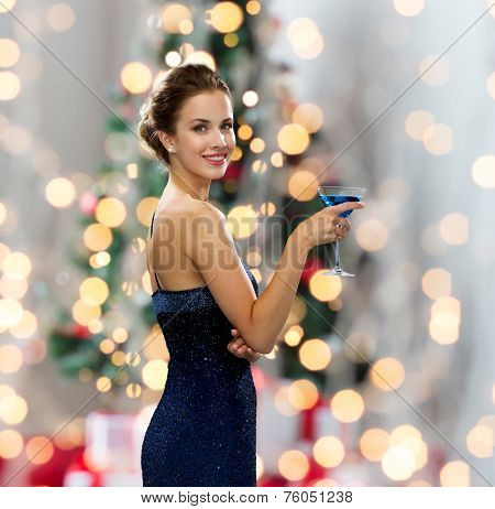 party, drinks, holidays, people and celebration concept - smiling woman in evening dress holding cocktail over christmas tree lights background