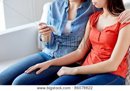 people, homosexuality, same-sex marriage, gay and love concept - close up of happy lesbian couple with smartphone at home