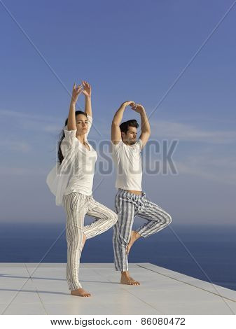 young couple practicing yoga at sunset in modern home terace with ocean and sunset in background