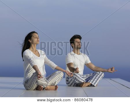 young couple practicing yoga at sunset in modern home terace with ocean and sunset in background