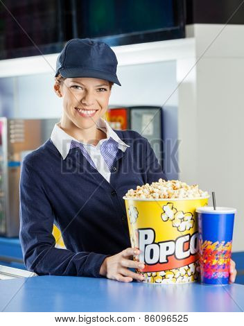 Portrait of smiling female worker with popcorn and drink at concession stand in cinema