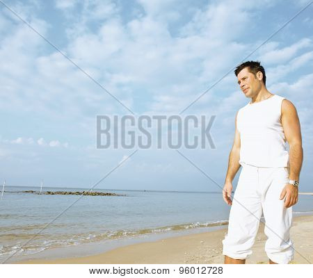 young brunette man on beach at sea smiling, gomosexual in white