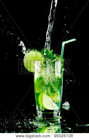 Pouring fresh mojito cocktail in glass isolated on black background