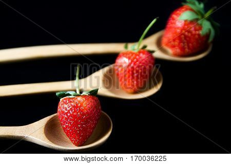 strawberry in wooden spoon on black background isolated
