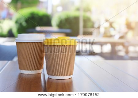 Two paper cups with tasty hot coffee on wooden table outdoors