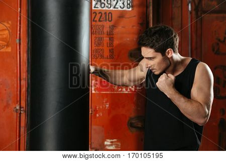 Photo of young concentrated strong boxer training in a gym with punchbag. Looking at punchbag.