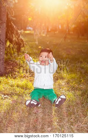 A small asian child plays in the Park sitting on the grass posing smiling. Little child holds the sunglasses