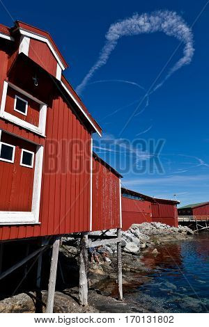 Summer Norwegian Landscape with red wooden fisherman cabin and blue sky with clouds