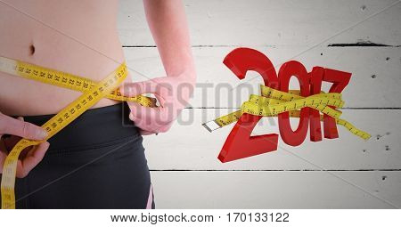 Mid-section of woman measuring her waist against 3D 2017 new year on wooden background
