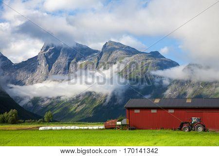 Small farm in Norway with tractor standing by a red barn wall