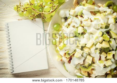 Fruit salad on a plate and sketchpad closeup. Flat lay. Copyspace